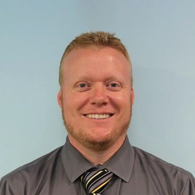 Chiropractor William Jackson Smiling In Front Of Blue Background